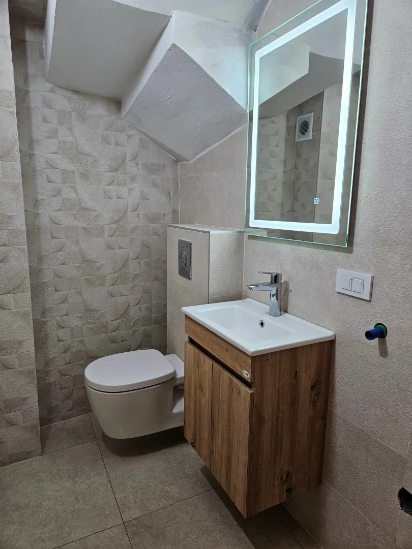 Modern bathroom equipped with a washbasin, toilet, and backlit mirror.