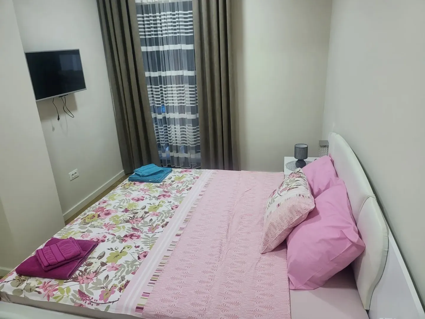 Bright bedroom featuring a double bed with pink bedding and a wall-mounted TV.