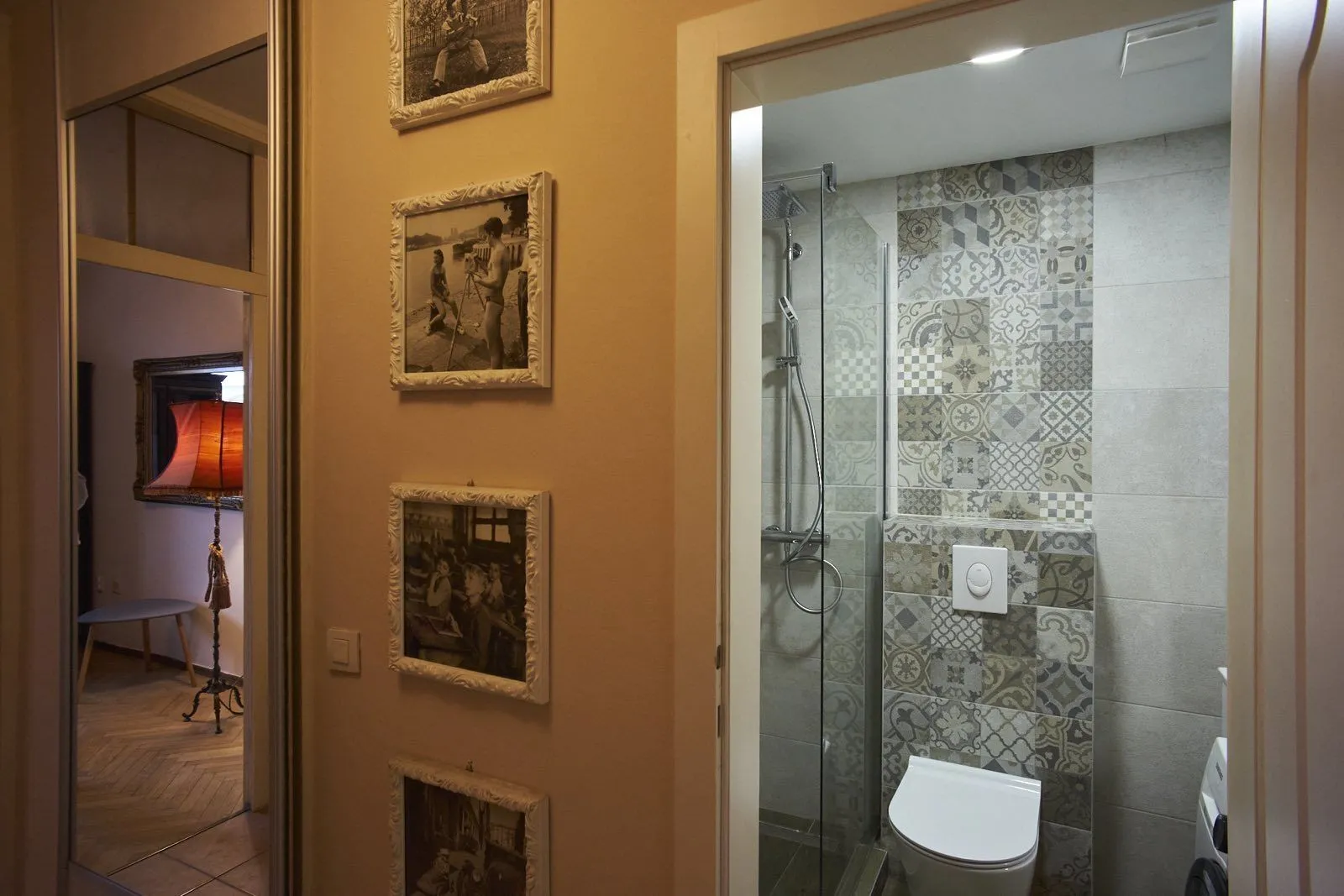 Pogled iz hodnika na moderno kupatilo sa tuš kabinom i ukrasnim pločicama.