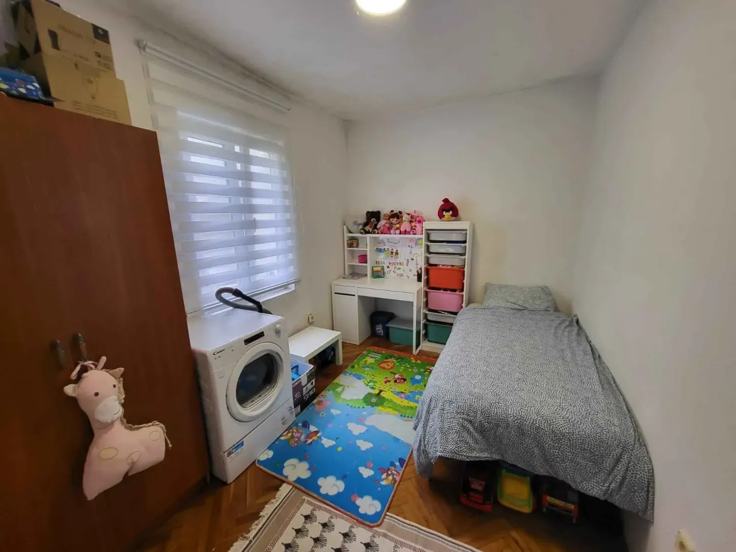 Dječja spavaća soba sa krevetom, radnim stolom i mašinom za pranje veša.