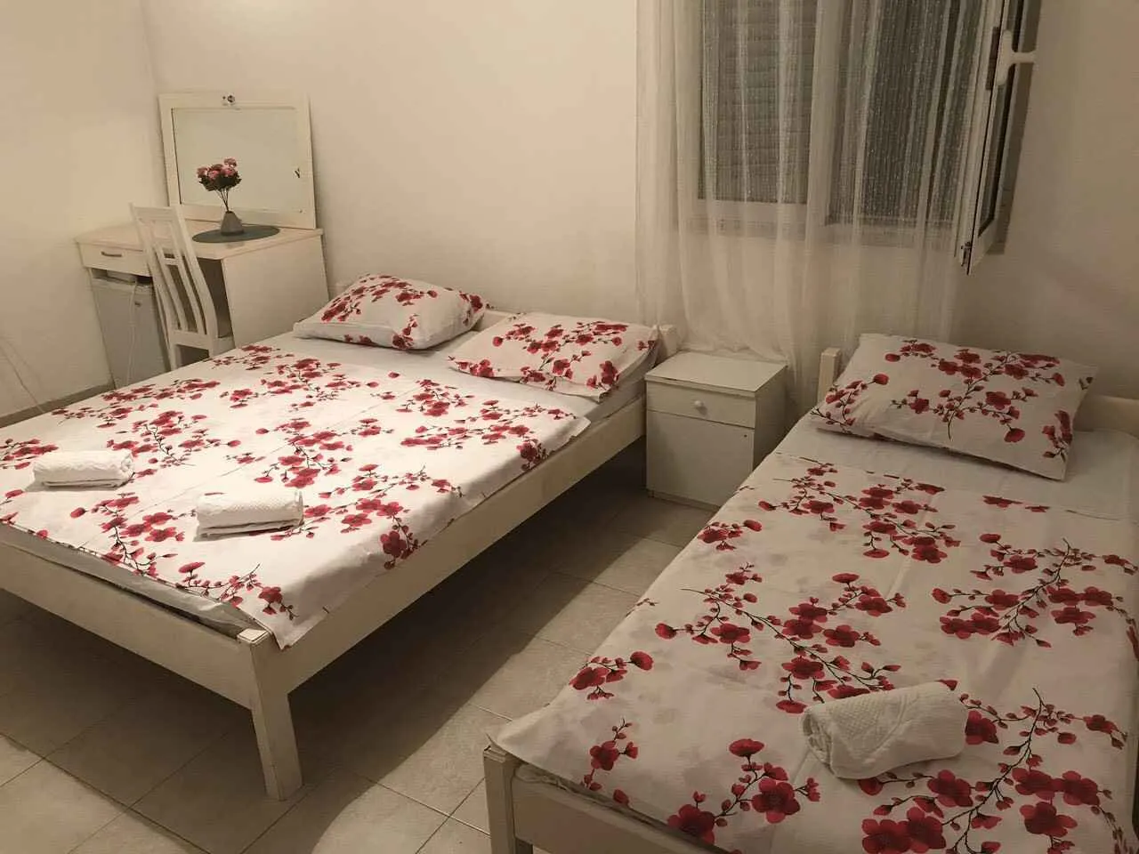Simple bedroom with two beds featuring floral bedding and a vanity desk.