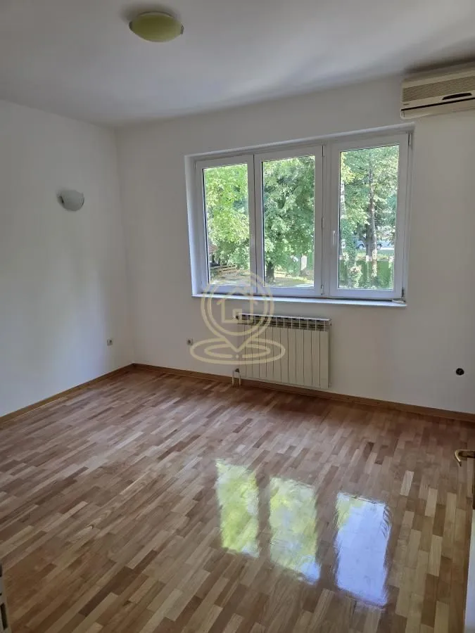 Empty room with hardwood floors and a window overlooking greenery.