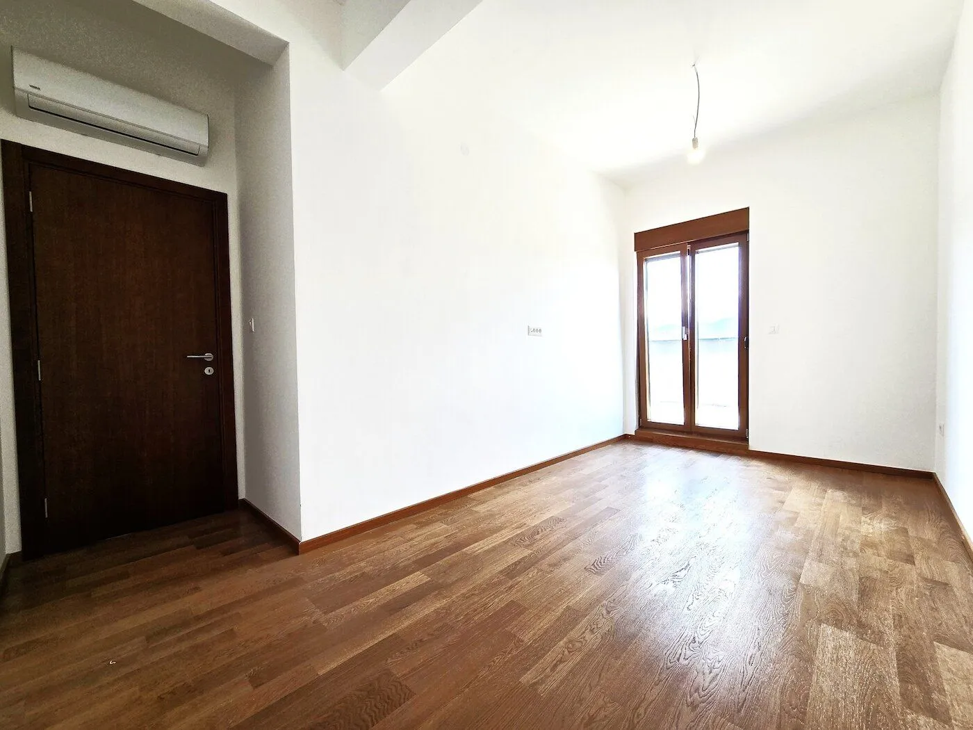 Empty room with wooden flooring and balcony doors.