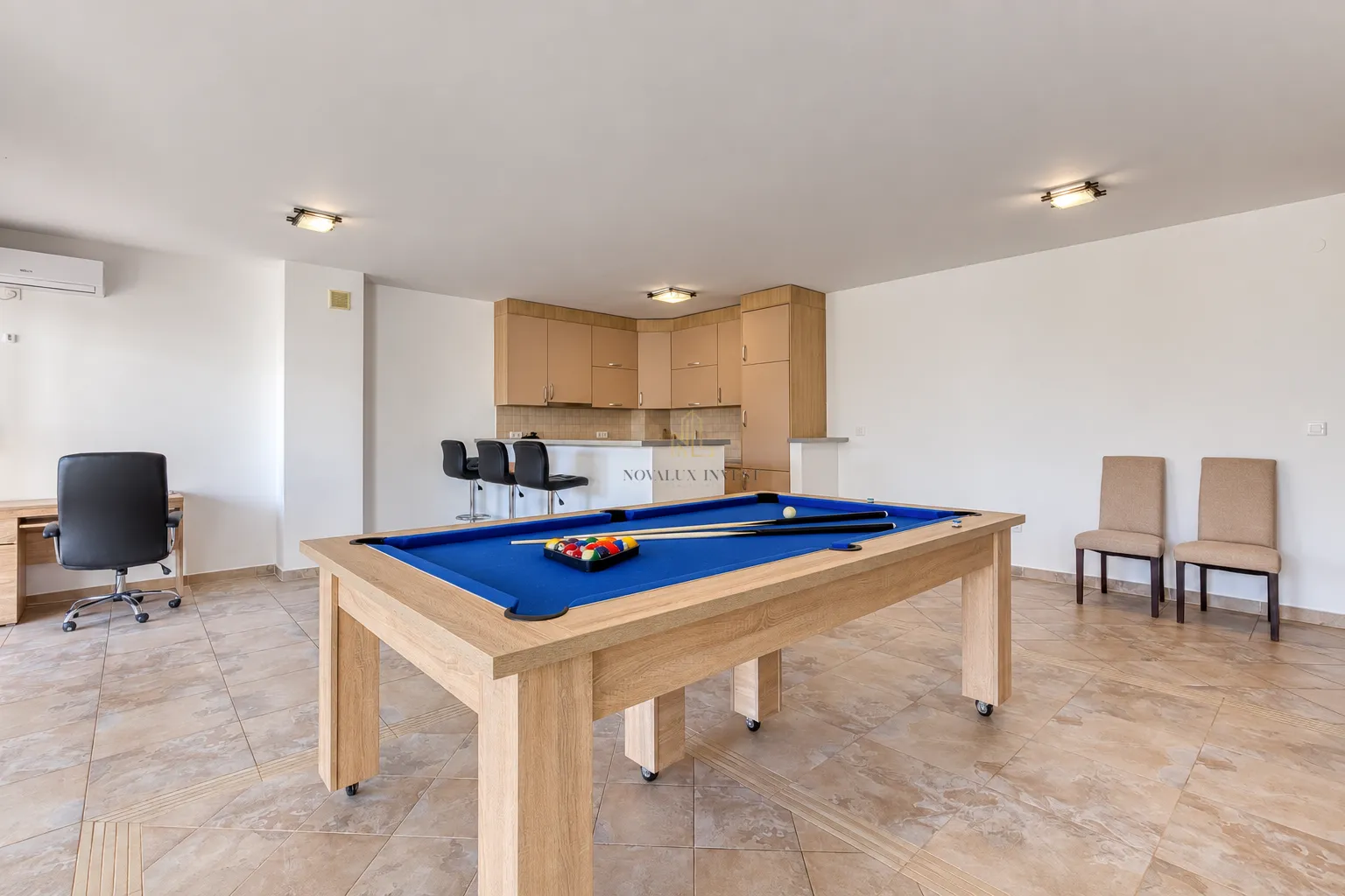 Spacious living room with a pool table and kitchen in the background.