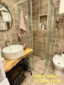 Kupatilo obloženo keramičkim pločicama sa tuš kabinom i umivaonikom na postolju od šivaće mašine. - image 7