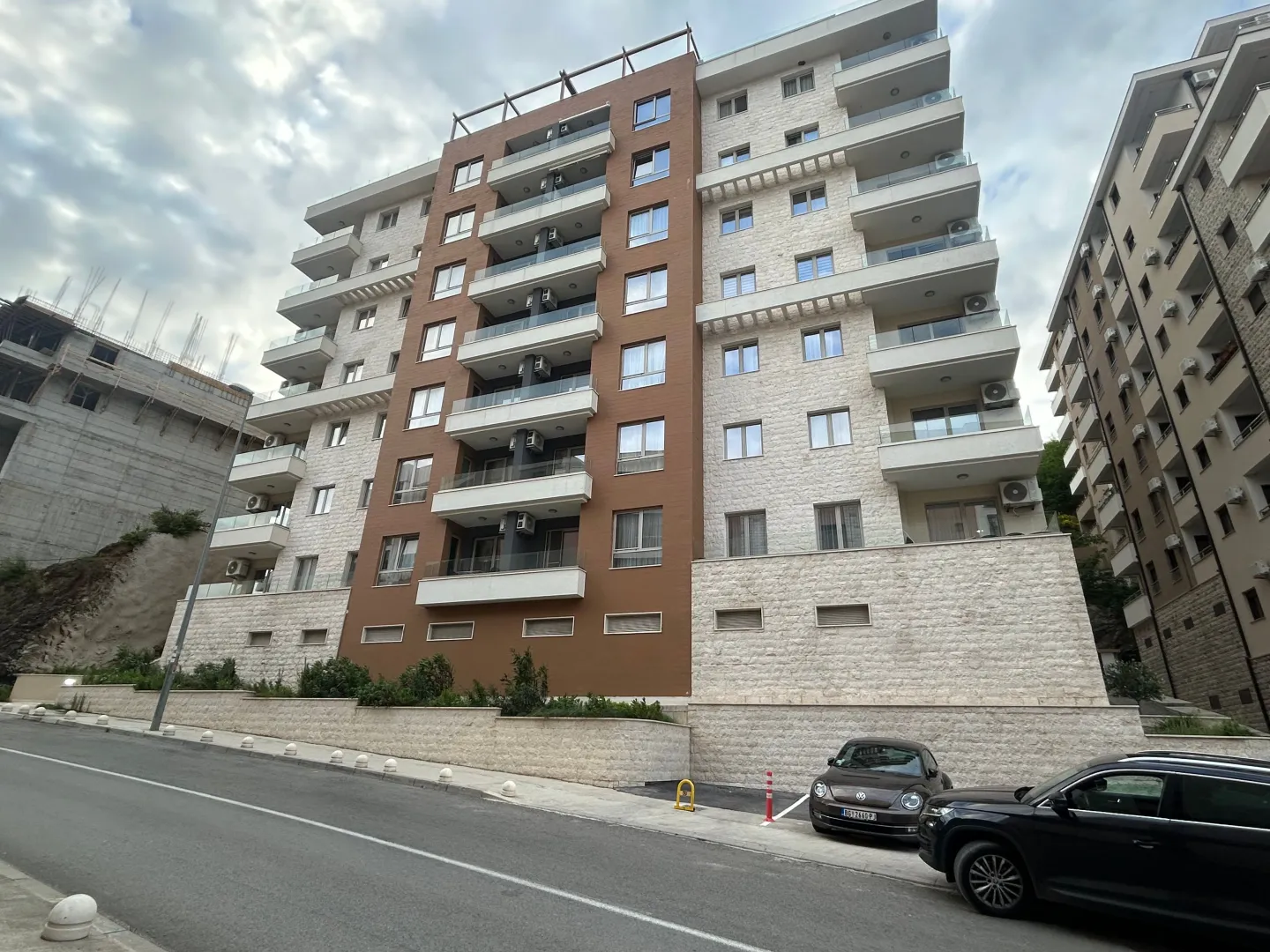 Exterior view of a modern multi-family apartment building with balconies and parking in front.