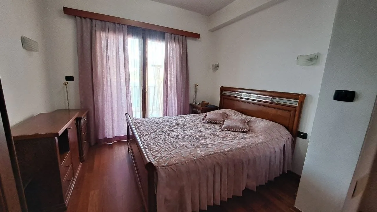 Spavaća soba sa bračnim krevetom, drvenim namještajem i zavjesama.