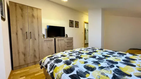 Spavaća soba sa bračnim krevetom, drvenim ormarom i komodom sa televizorom. - image 6