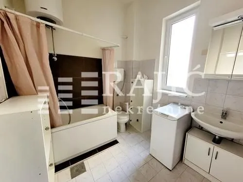 Smaller bathroom with a bathtub, washbasin, and washing machine.