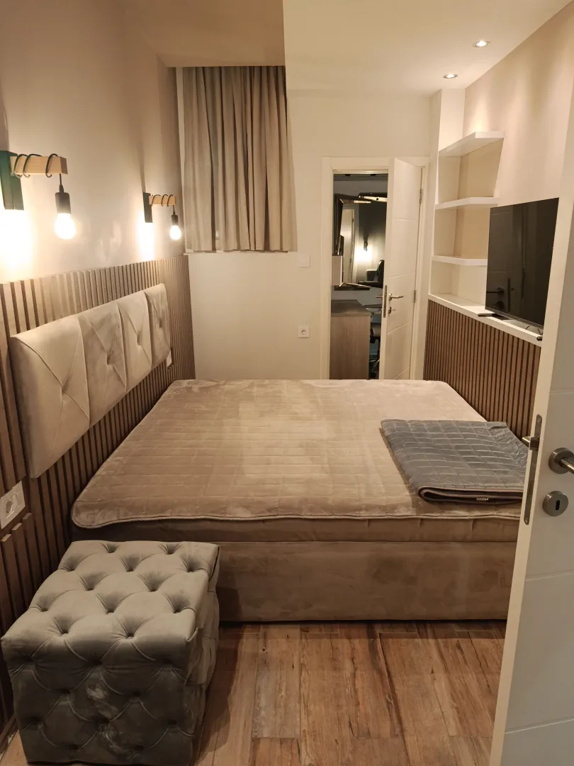 Modern bedroom with a double bed, wooden wall panels, and a TV.