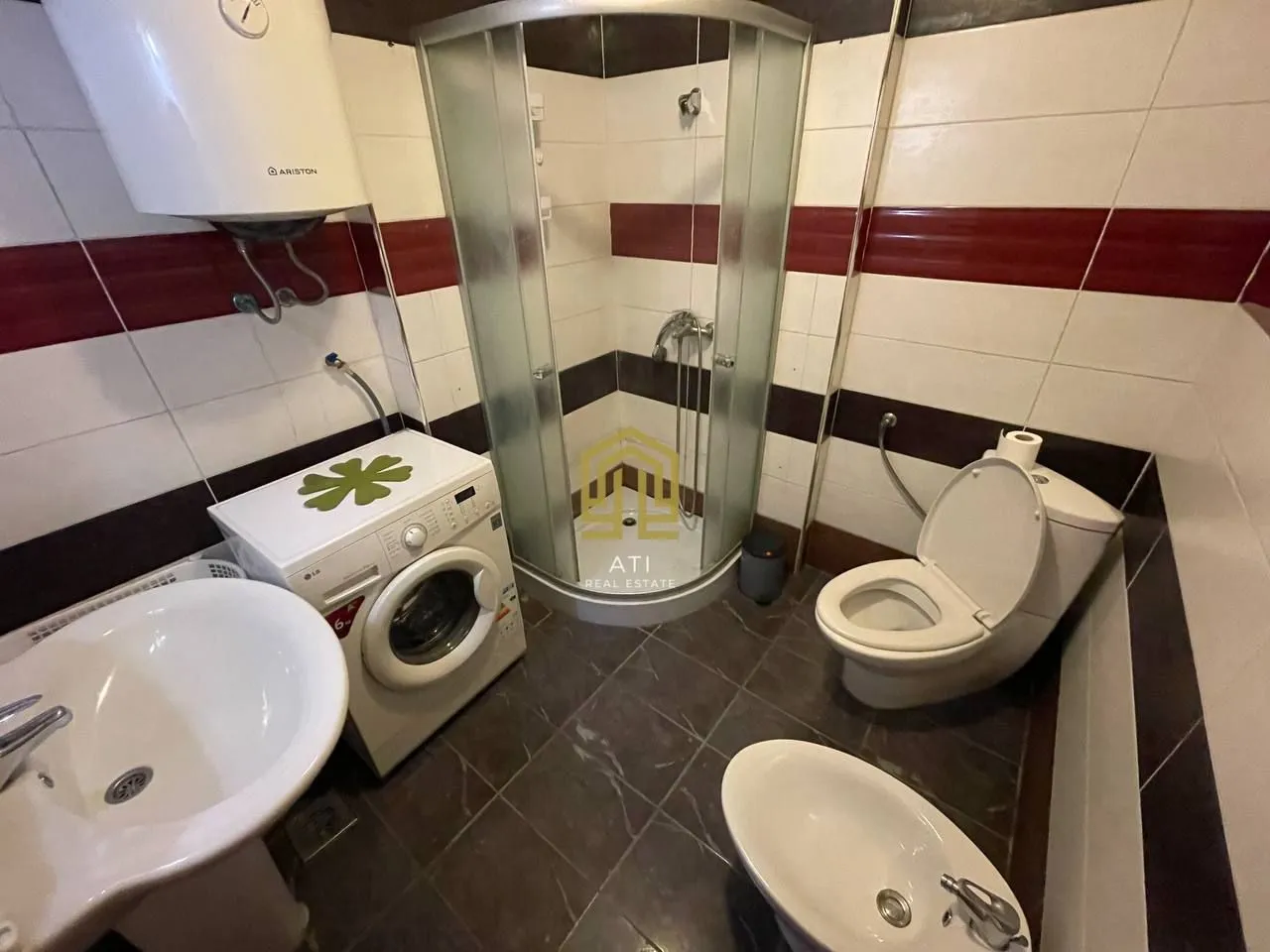 Small bathroom with a shower cabin, washbasin, washing machine, and toilet.