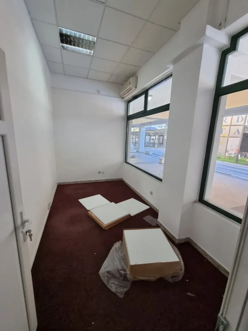 Empty commercial space with large windows and dark carpet.