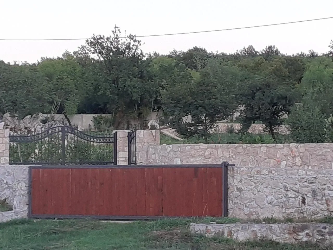 Stone fence with a courtyard gate and greenery in the background.