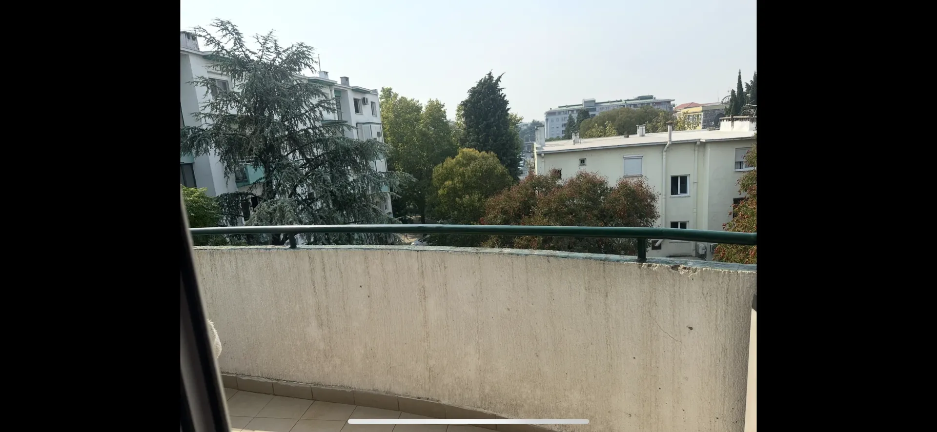 Pogled sa balkona na okolne zgrade i drveće.