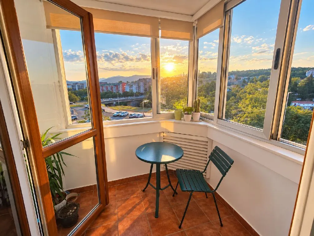 Zastakljeni balkon sa malim stolom, stolicom i pogledom na grad.