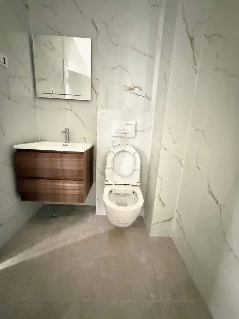 Modern bathroom with a sink, mirror, and toilet bowl clad in marble tiles.