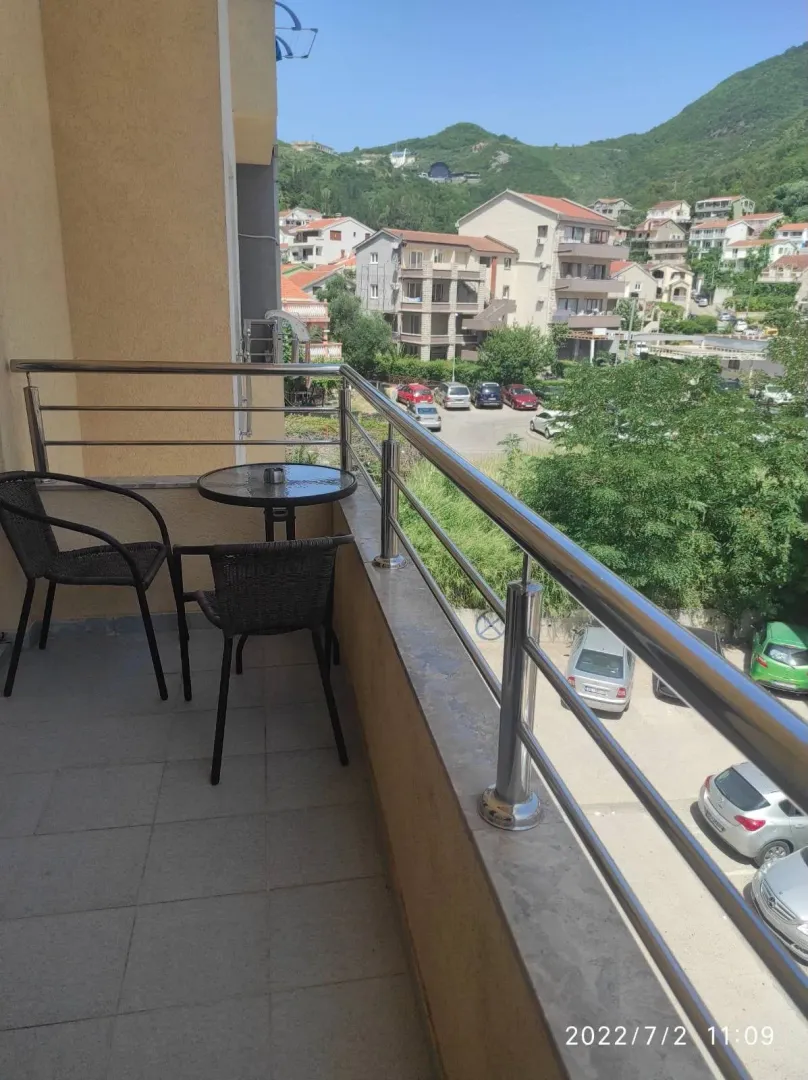 Small furnished balcony with a table and two chairs and a view of the neighborhood.
