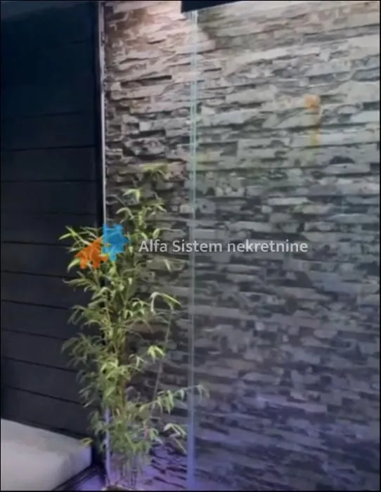 Detalj enterijera sa dekorativnim kamenim zidom i biljkom.