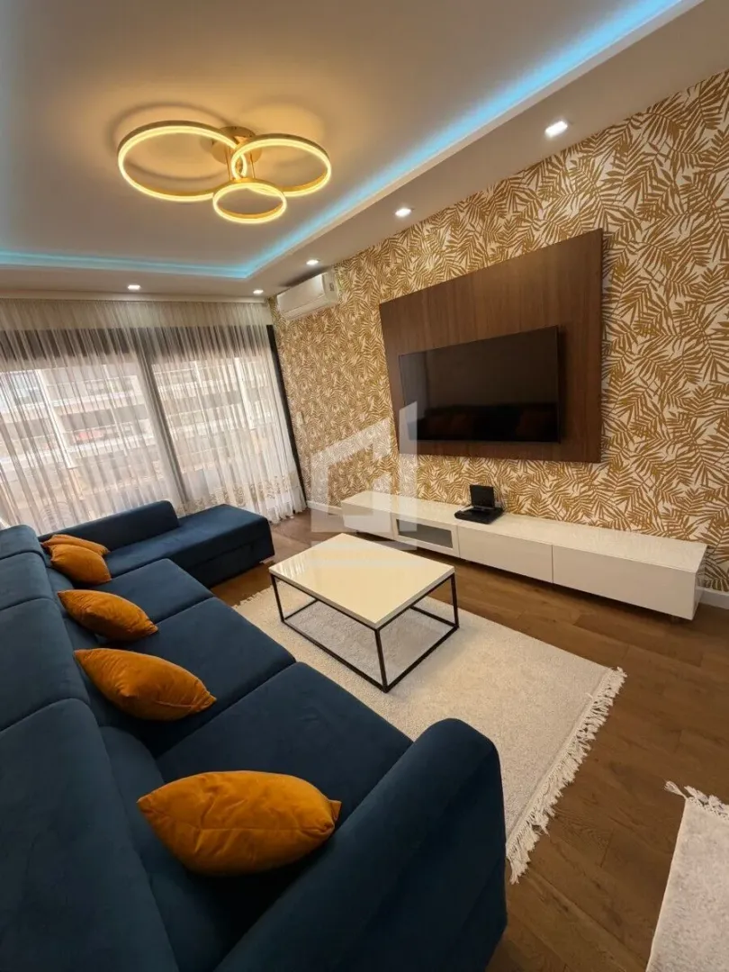 Modern living room with a blue sectional sofa, TV, and decorative wallpaper.