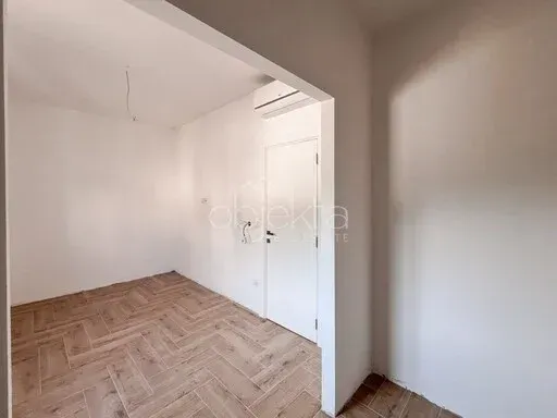 Prazna soba sa parketom i bijelim zidovima.