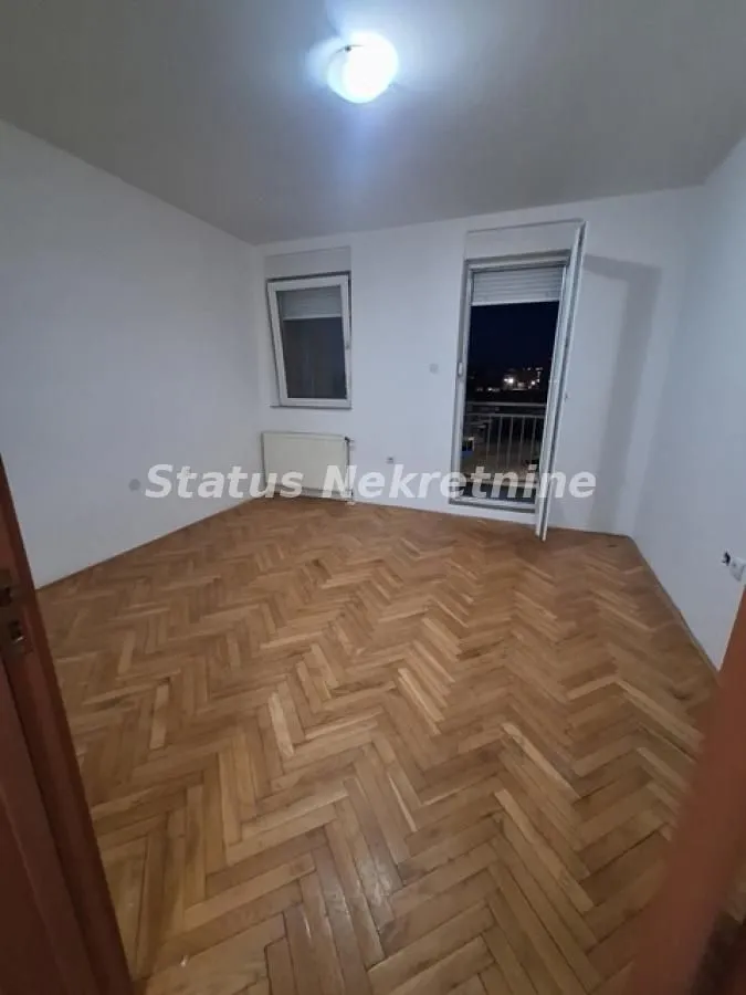 Prazna soba sa parketom i izlazom na balkon.