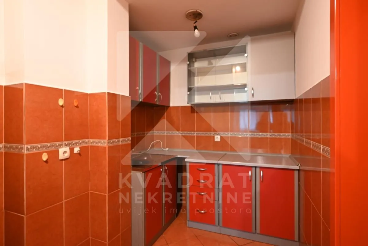 Small kitchen with red cabinets and warm-toned wall tiles.