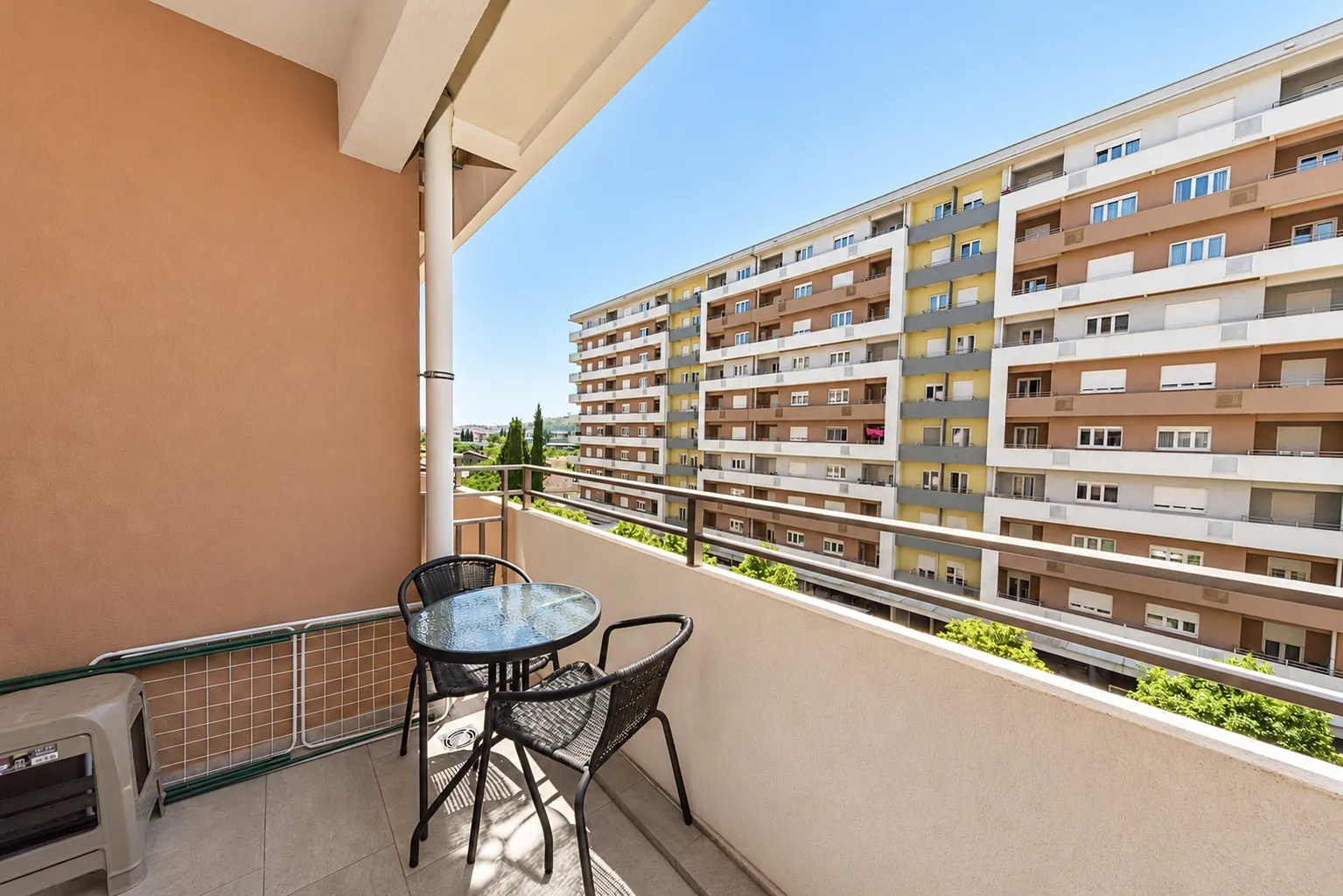 Furnished balcony with a table, chairs, and a view of the neighboring building.