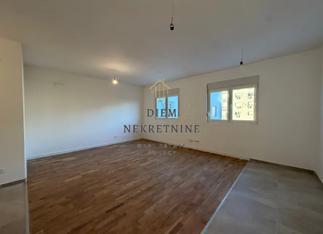 Empty room with wooden flooring and windows.