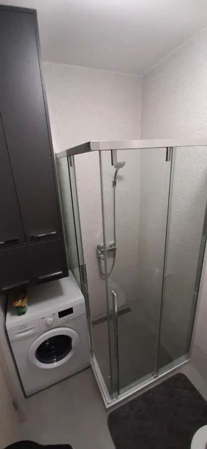 Bathroom with a shower cabin, washing machine, and dark cabinetry.