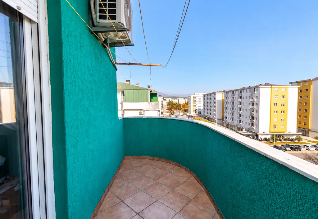 Zastakljeni balkon sa pogledom na okolne zgrade.