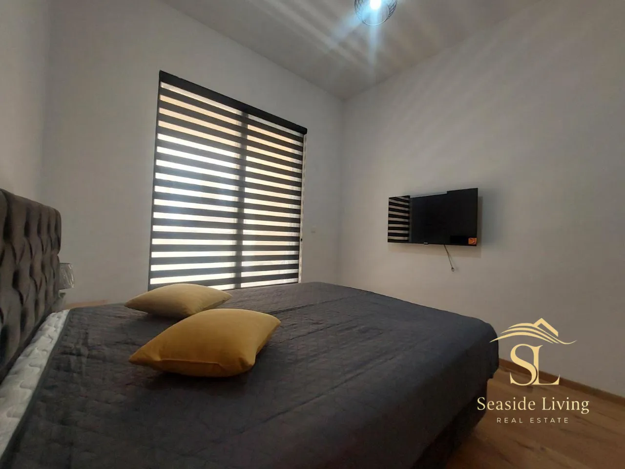 Furnished bedroom with a double bed, TV, and window blinds.