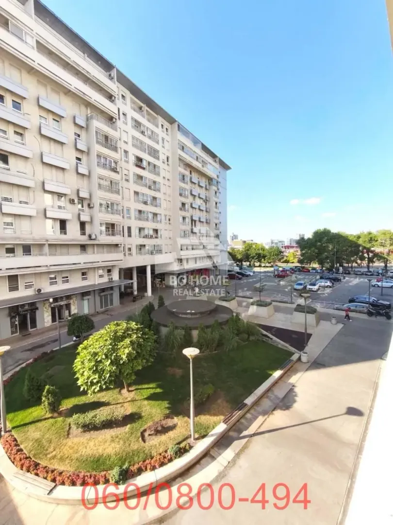 Pogled sa terase na okolne zgrade, parking i uređeno zelenilo.