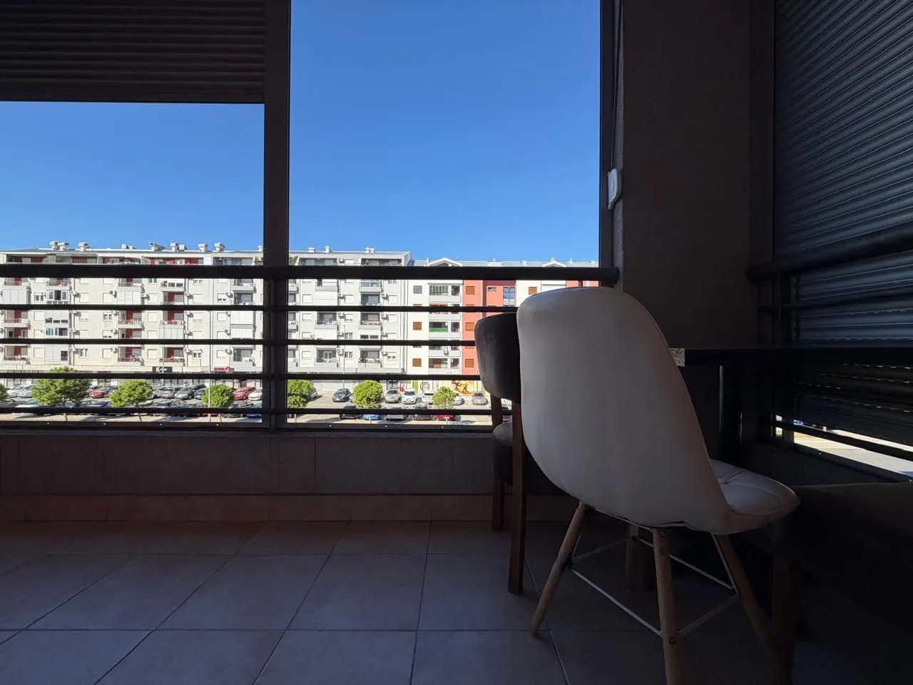 Covered terrace with a table, chairs, and a view of surrounding buildings and parking.