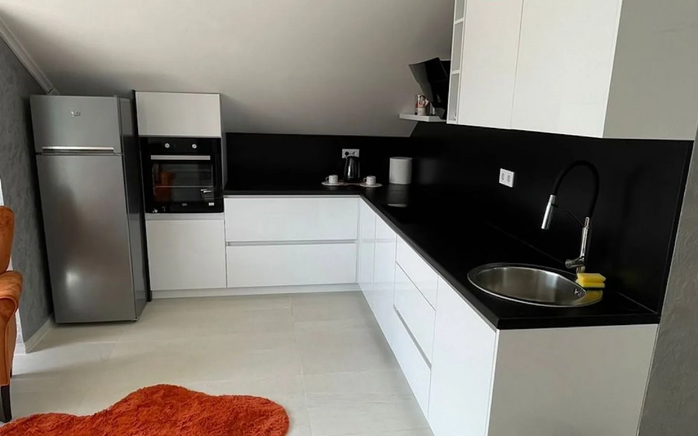 Modern attic kitchen with white units and a black countertop.