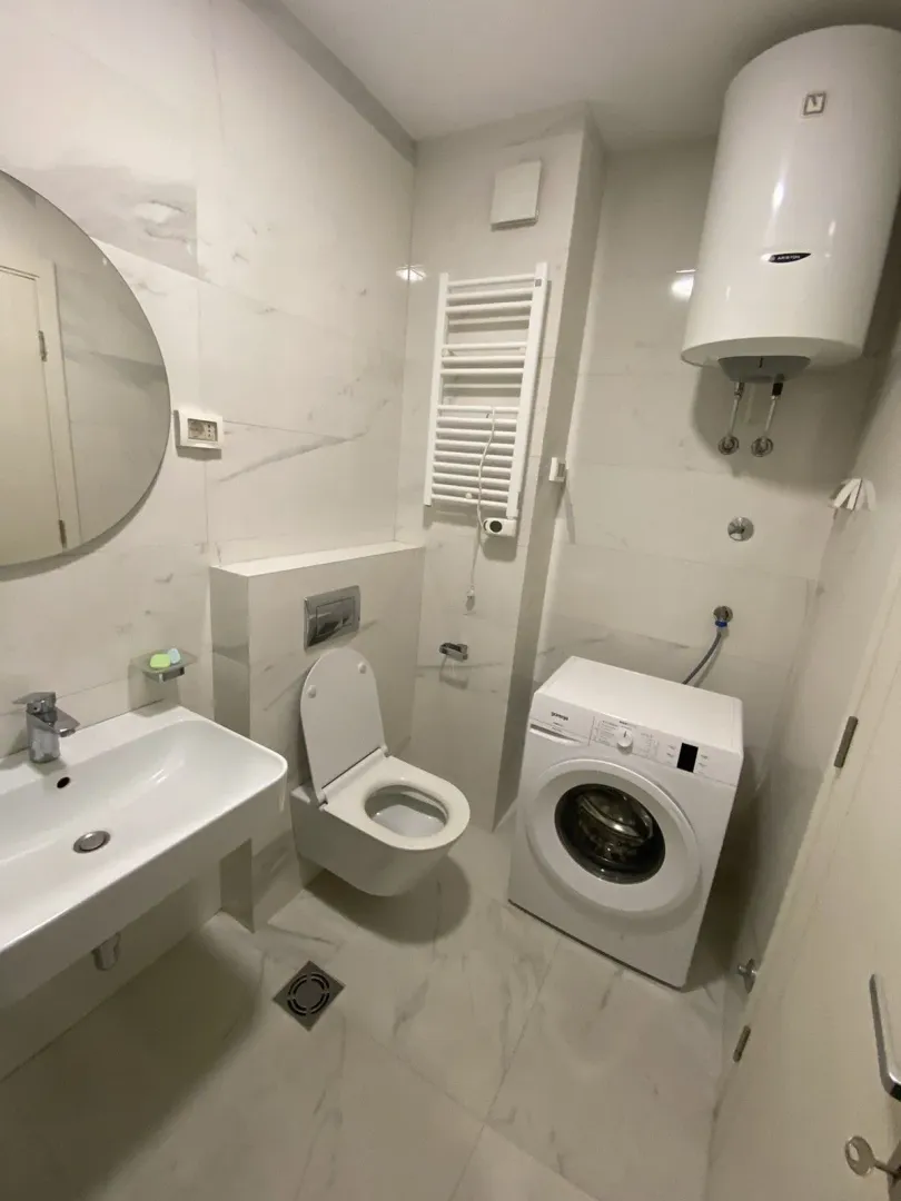 Bright bathroom with a washing machine, water heater, and modern fixtures.