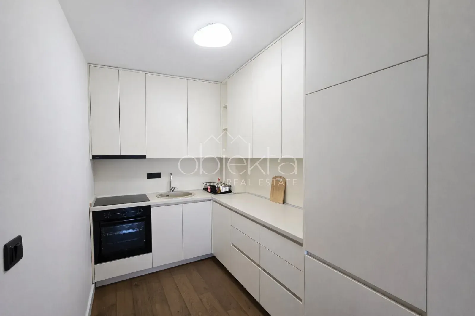 Modern white kitchen with built-in appliances and wooden flooring.