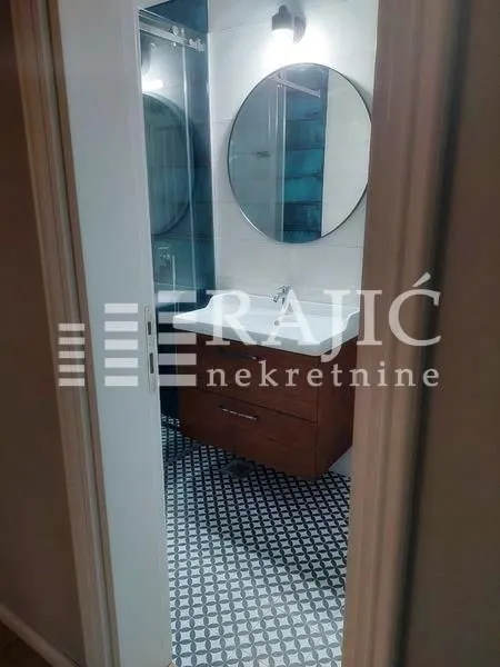 View of a modernly decorated bathroom with a washbasin and a round mirror.