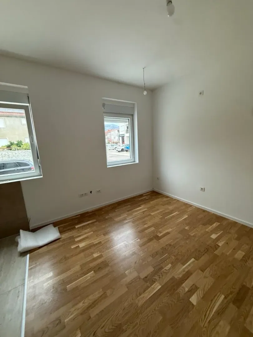 Prazna soba sa parketom i bijelim zidovima.