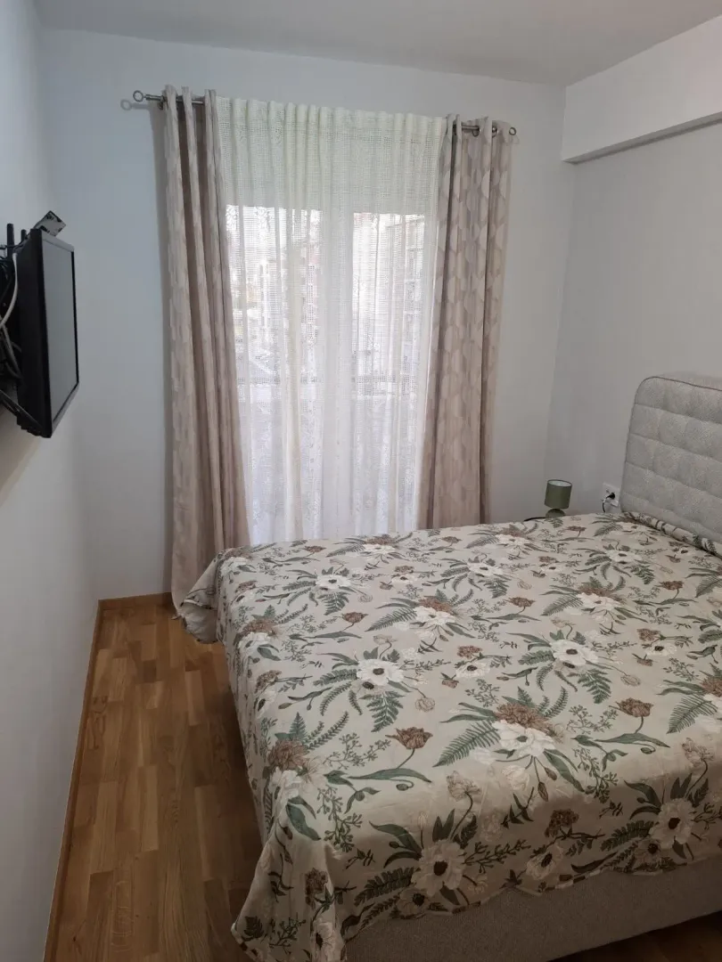 Namještena spavaća soba sa bračnim krevetom i prozorom sa zavjesama.
