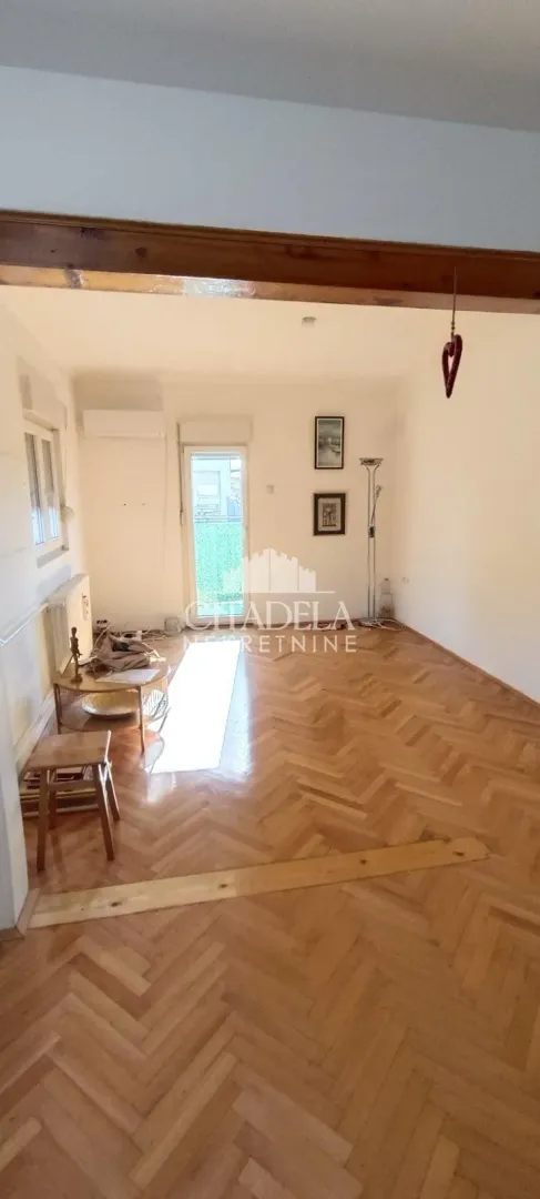 Prazna dnevna soba sa parketom u riblju kost i izlazom na terasu.