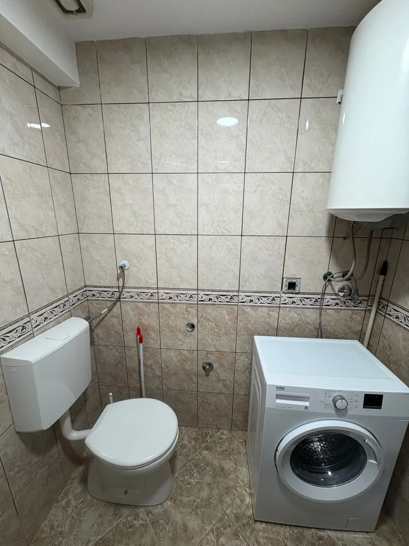 Smaller bathroom tiled with ceramic tiles containing a toilet bowl and washing machine.