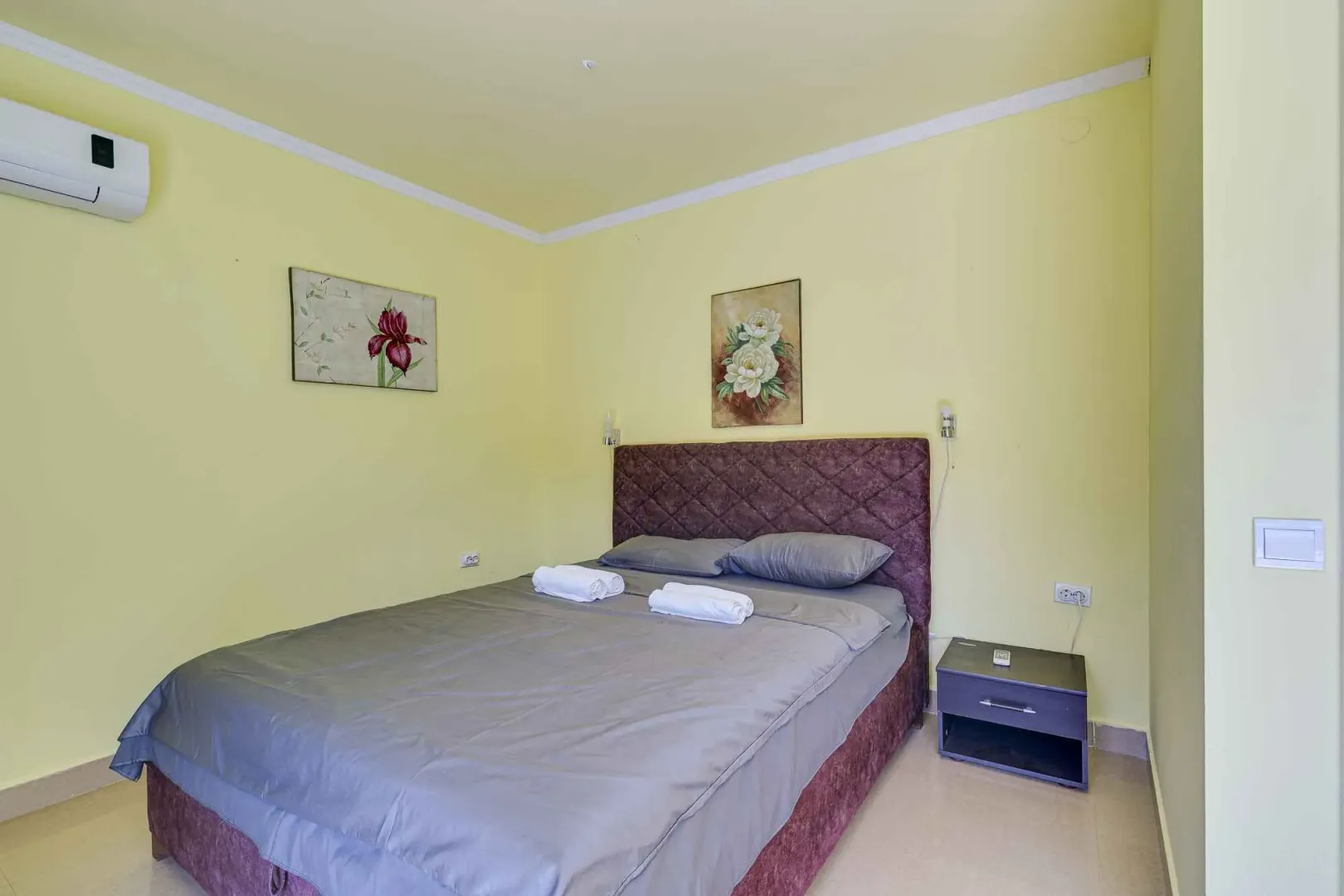 Spavaća soba sa bračnim krevetom, žutim zidovima i klima uređajem.