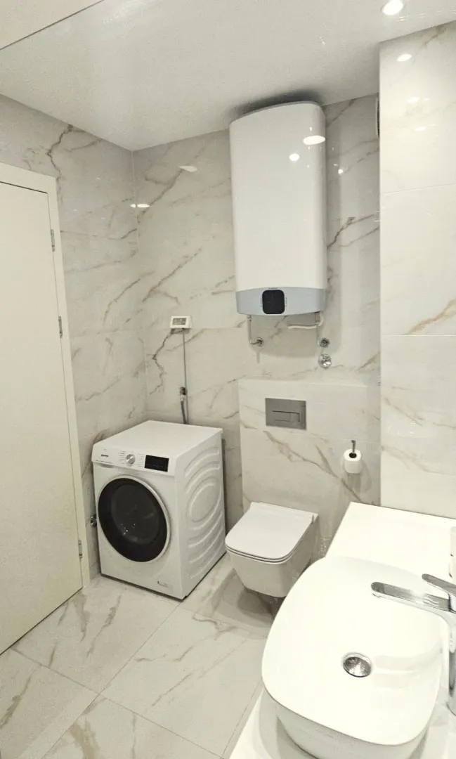 Modernly equipped bathroom with washing machine, toilet bowl and washbasin.