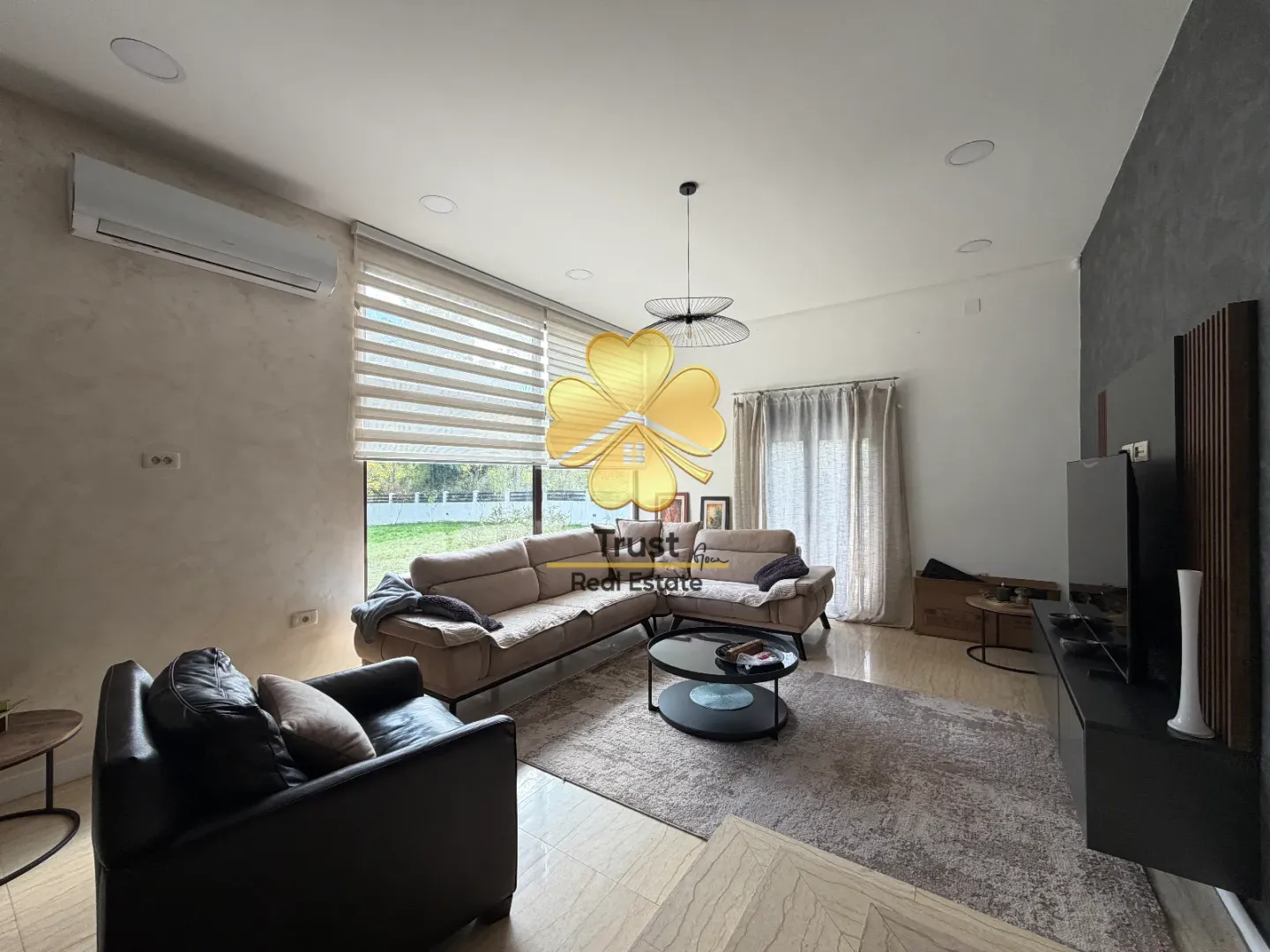 Spacious living room with a sofa set, TV unit, and large windows.