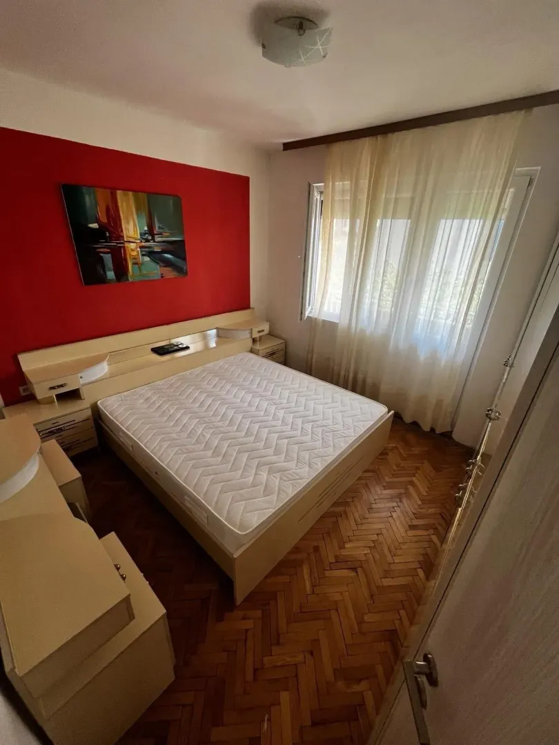 Svijetla spavaća soba sa crvenim akcentnim zidom i parketom.
