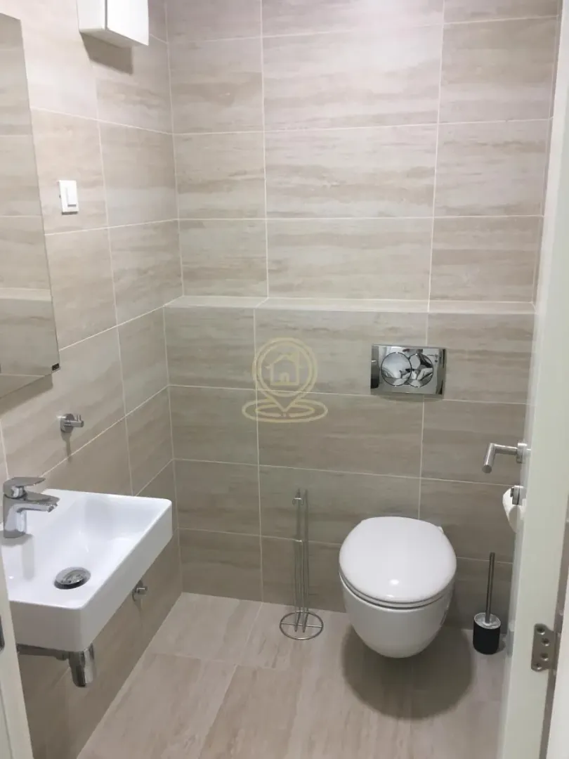 Smaller bathroom tiled in beige tones with a washbasin and toilet.