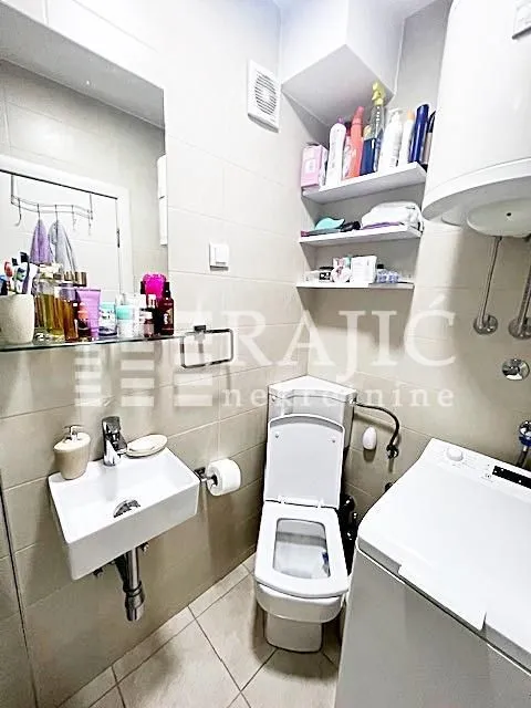 Small bathroom with a sink, toilet, washing machine, and shelving units.