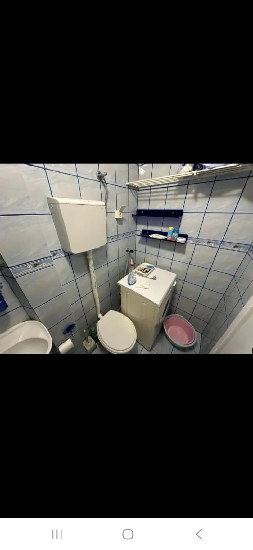 Manje kupatilo sa pločicama u plavim tonovima, wc šoljom i veš mašinom.