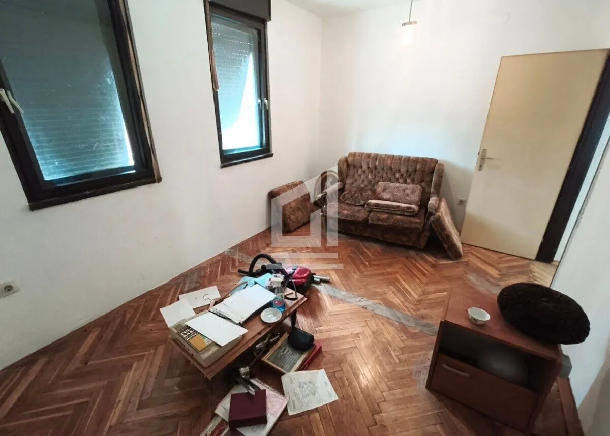 Living room with wooden parquet flooring, sofa, and scattered items on the floor.
