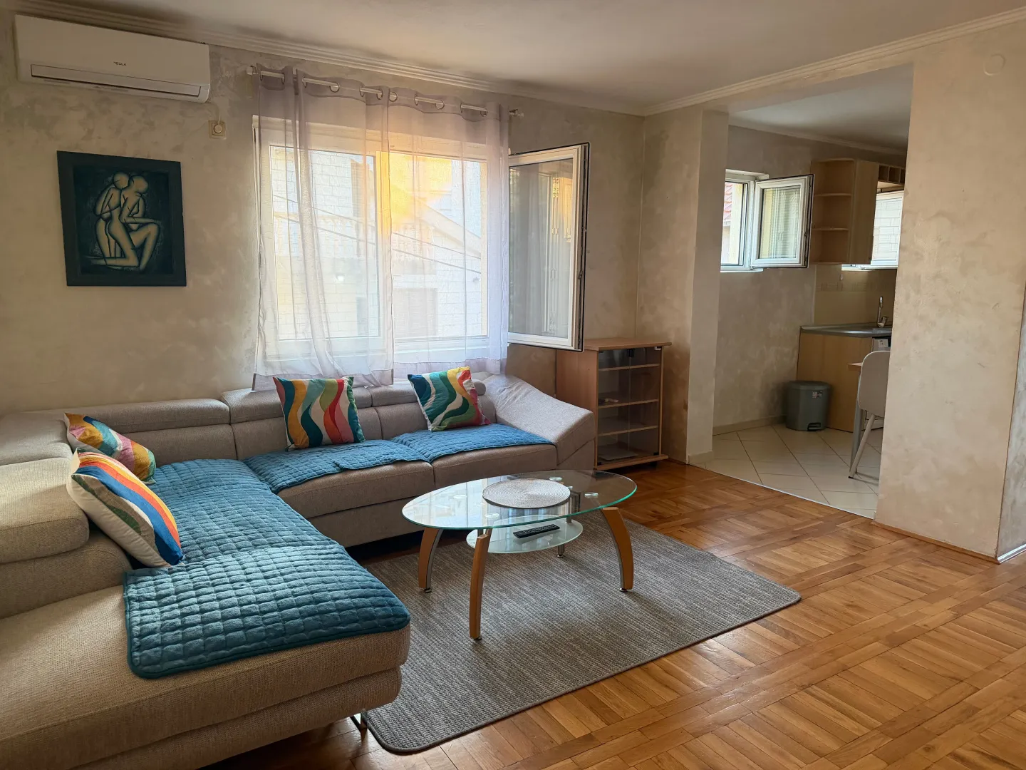 Living room with a corner sofa, glass coffee table, and a view of the kitchen.